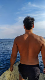 Rear view of shirtless man standing at beach against sky