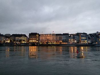 River by illuminated buildings against sky at dusk