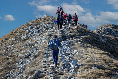 Group of hikers walk on the mountain path, helping themselves up the climb with trekking poles.