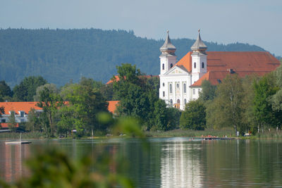 Trees by lake against buildings