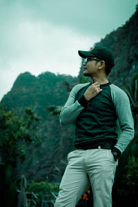 Young man looking away while standing against mountain