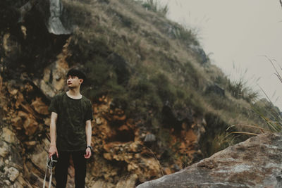 Thoughtful young man with camera standing on rock