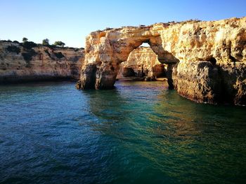 Rock formations by sea against clear blue sky