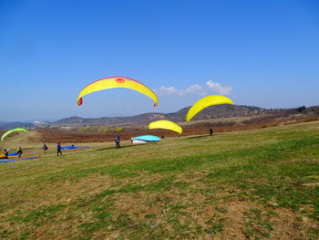 People flying over field against sky