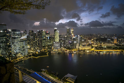 Illuminated buildings by river against sky in city at night