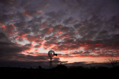 Silhouette traditional windmill on field against cloudy sky during sunset