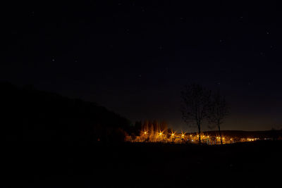 Silhouette trees on landscape against sky at night