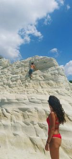 Side view of woman looking at man climbing on white rock of scala dei turchi