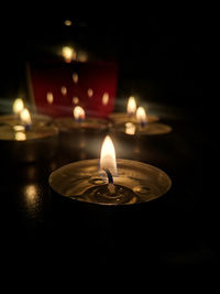 Close-up of lit tea light candles in darkroom