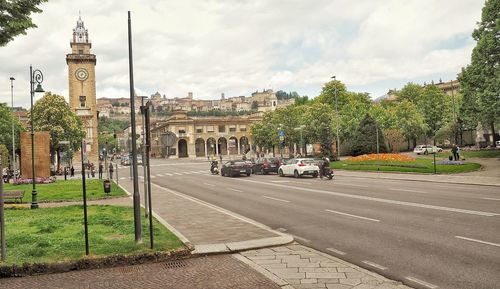 Road by trees and buildings against sky