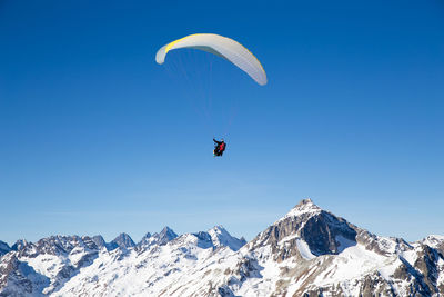 Person paragliding over snowcapped mountain against sky