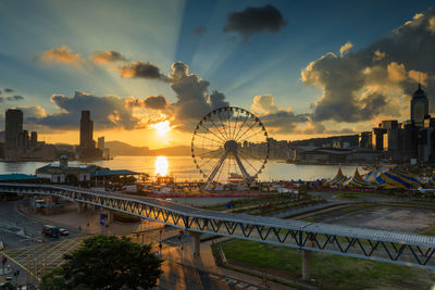 Ferris wheel by river against sky during sunset