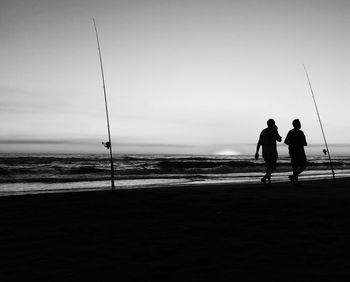Silhouette people on beach against clear sky