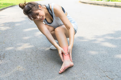 Full length of young woman holding her foot while crouching on road