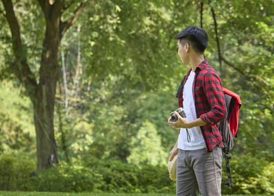 Young man looking at camera while standing on tree in forest
