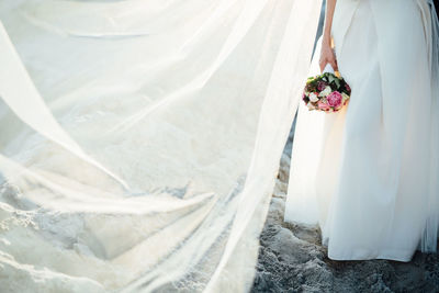 Low section of woman holding bouquet at beach