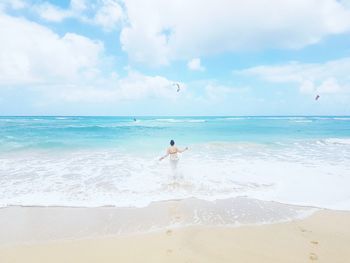 Rear view of woman standing in sea against cloudy sky