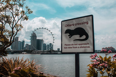 Information sign by river against sky in city