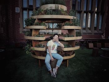 Young man yawning while sitting on seat by plants at yard