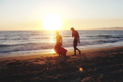 Silhouette people walking on beach against clear sky during sunset