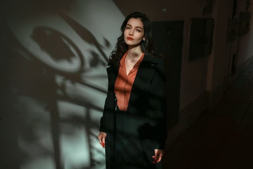 one person, adult, women, fashion, young adult, standing, black, portrait, architecture, clothing, darkness, indoors, brown hair, hairstyle, human face, looking at camera, serious, female, looking, three quarter length, dark, emotion, jacket, business, lifestyles, city, front view, wall - building feature, copy space, person, waist up, shadow