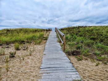 Boardwalk on grassy field against sky