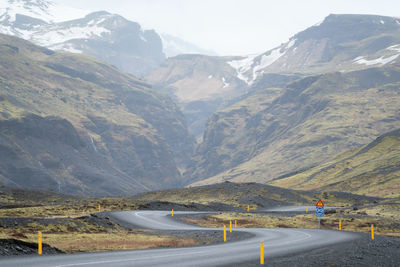 Country road leading towards mountains against sky