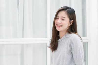 Portrait of smiling woman standing against window