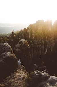 Rear view of man standing on rock against sky