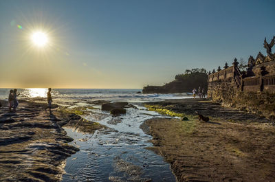 People at beach by tanah lot against sky
