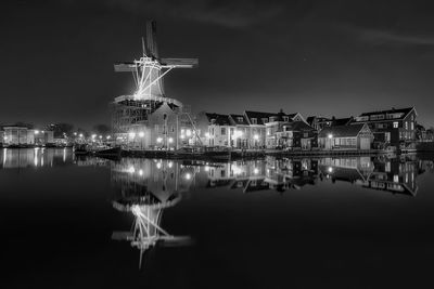 Reflection of illuminated traditional windmill and houses on calm lake at night