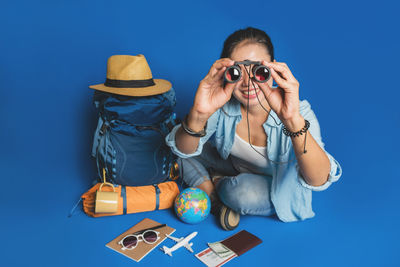 Portrait of young woman sitting against blue background