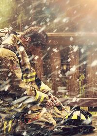 Side view of firefighter kneeling on road during snowfall