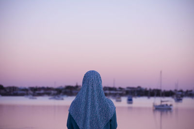 Rear view of woman standing in river against sky during sunset