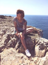 Full length of woman sitting on rock by sea against clear sky