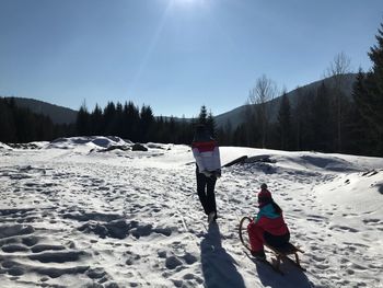 Mother pulling sled with daughter on snow covered field