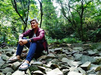 Full length of man sitting on rock in forest