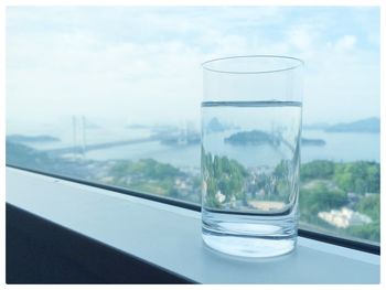 Drinking glass on window sill by sea against sky