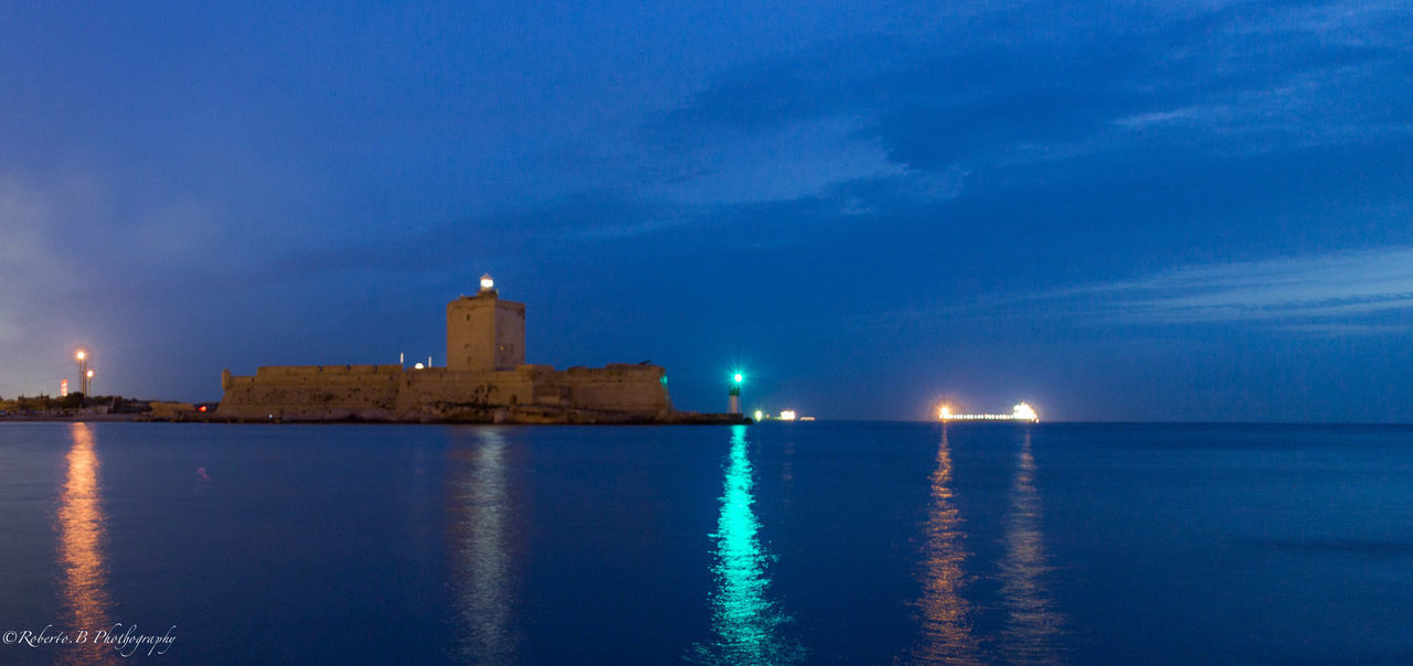 water, illuminated, sea, sky, blue, waterfront, night, reflection, building exterior, architecture, built structure, scenics, dusk, tranquility, tower, tranquil scene, outdoors, nature, beauty in nature, city