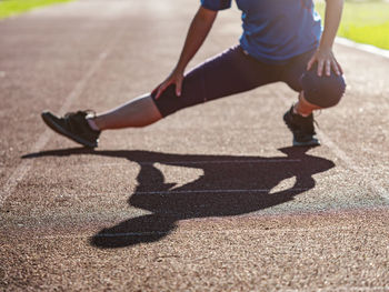 Middle age woman stretching legs and body before run during sunny morning on stadium