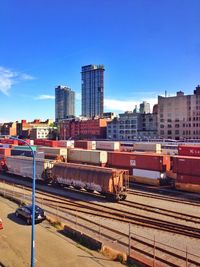 Trains on railroad tracks in city against blue sky