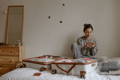 Young woman with open suitcase on the bed at home