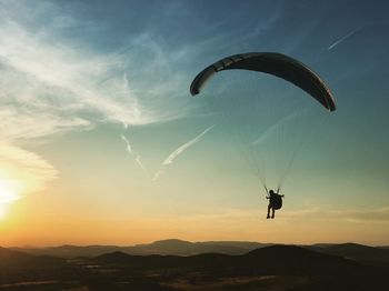 Silhouette man paragliding against sky during sunset