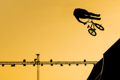 Low angle view silhouette of man performing stunts on bicycle against sky during sunset