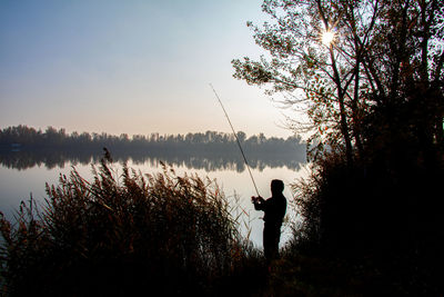 Man fishing by lake against sky