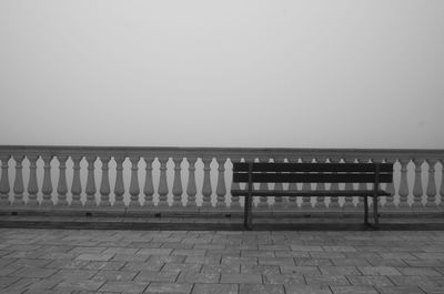 Empty bench by sea against clear sky