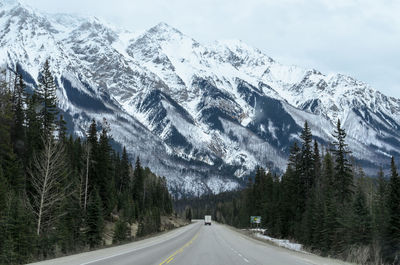 Snow covered road by mountains against sky