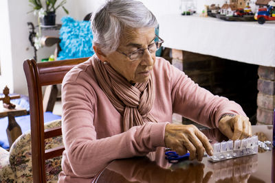 Senior woman taking medicine while sitting by table at home