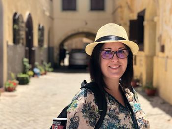 Portrait of smiling woman wearing hat while standing against buildings in city