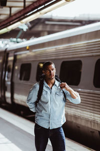 Male tourist carrying backpack by train looking away on railroad station